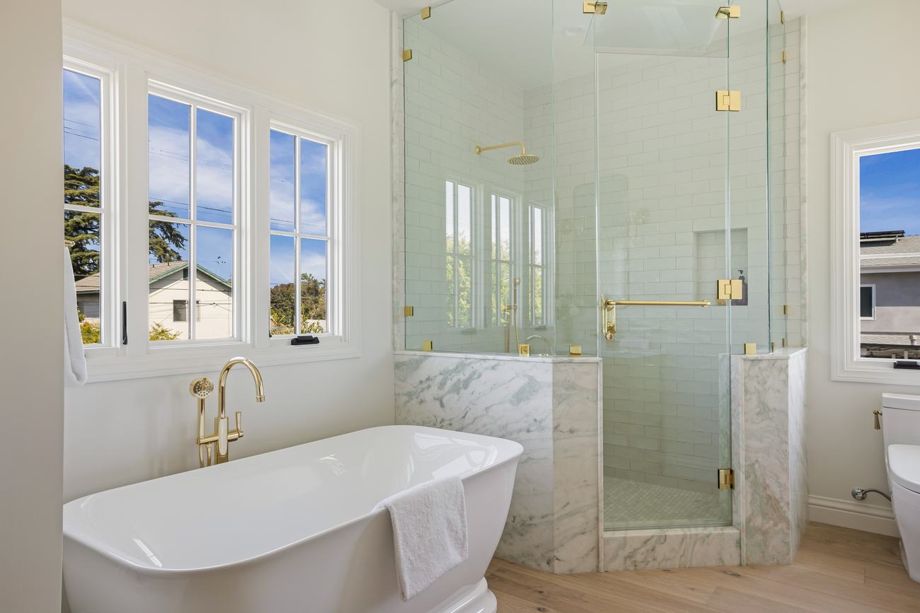 Glass shower detail with brass fixtures and marble half-wall