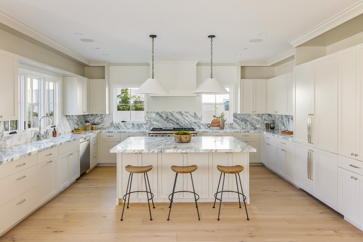Large kitchen island in white marble with black hardware and pendant lighting