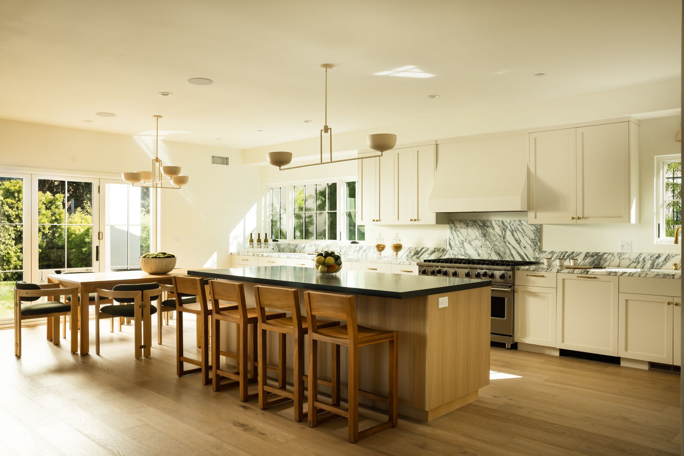 Sunlit kitchen and dining island at 23rd Street, white oak cabinetry with a black stone island and marble backsplash